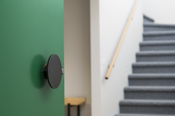 Green door with round handle next to carpeted stairs.