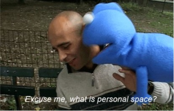 Blue puppet whispering to a smiling man on a park bench.