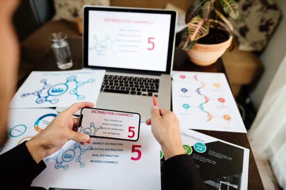 Person reviewing distribution channels on laptop and documents at a desk.