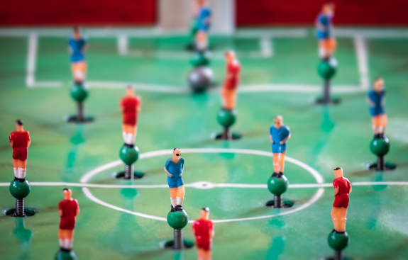 Close-up of foosball table with red and blue player figures on green field.