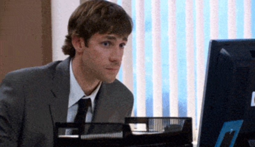 Man in office suit looking at computer screen with blinds in background
