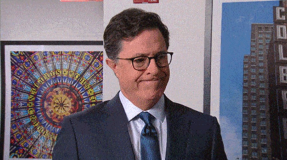 Man in a suit making a face in front of a colorful poster.