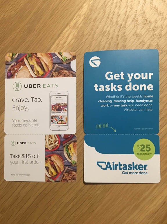 Uber Eats and Airtasker promotional cards on wooden table.