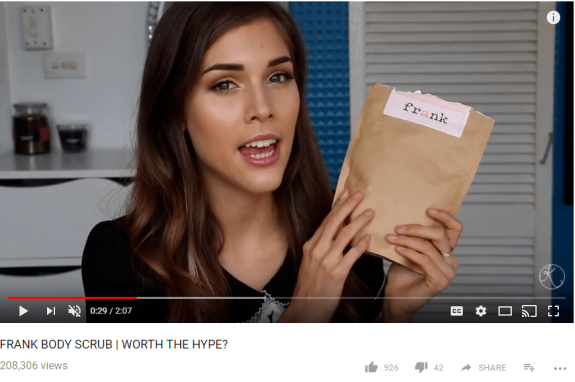 Woman holding Frank Body Scrub pouch during a review video.