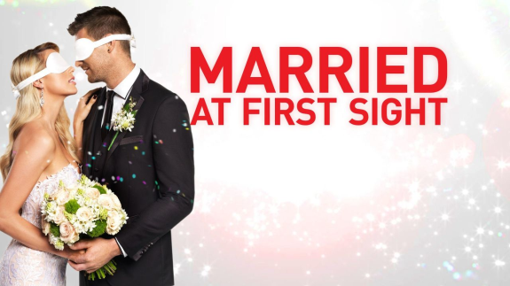 Blindfolded couple in wedding attire holding bouquet with 'Married at First Sight' text.