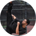 Man performing a high kick in black outfit outdoors on a sunny day.