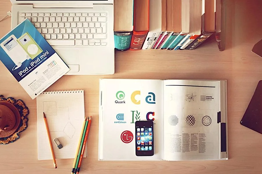 Office desk with laptop, books, smartphone, and stationery items.