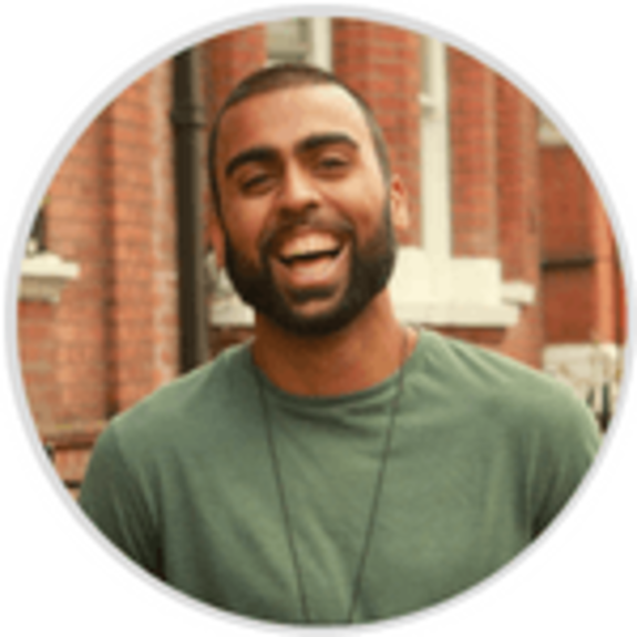 Man in green shirt smiling against brick wall background.
