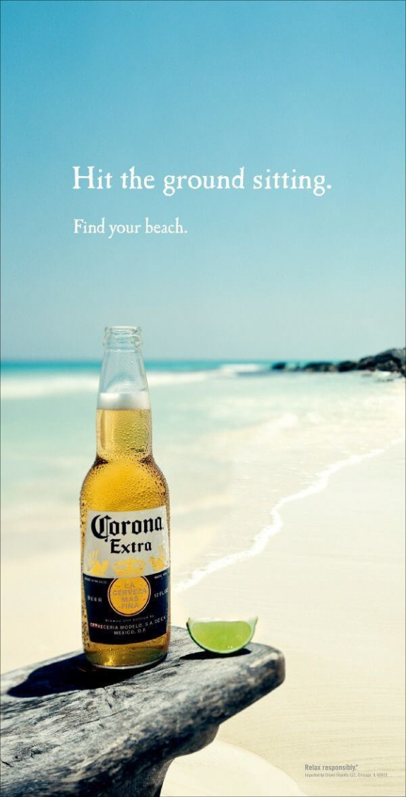 Corona Extra beer bottle with lime slice on a beach with blue sky.