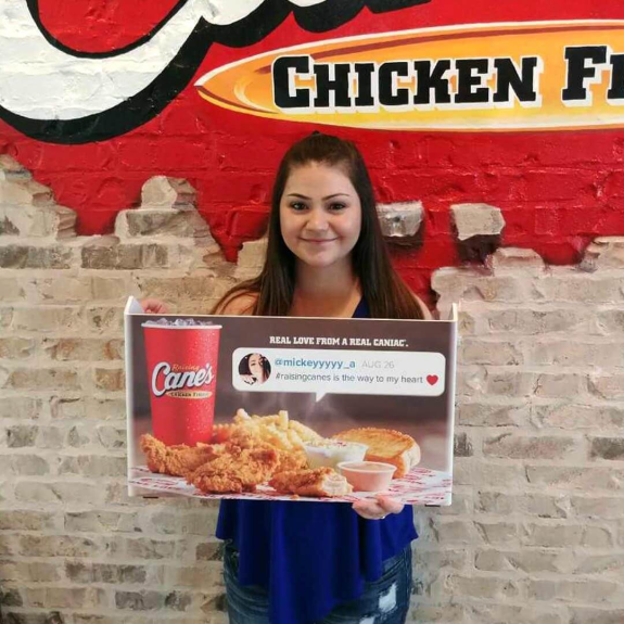 Woman holding Raising Cane's sign featuring chicken fingers and drink