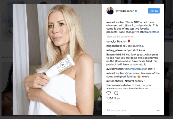 Woman holding skincare product wrapped in a white towel in a bathroom.