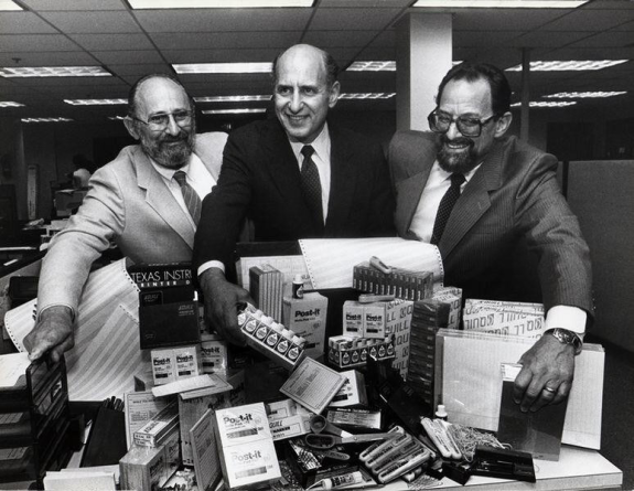 Three businessmen in suits smiling with office supplies on a desk in a vintage office.