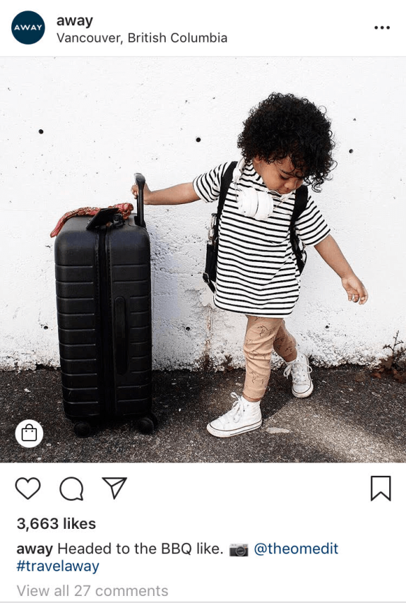 Child in striped shirt with suitcase and headphones standing outdoors.