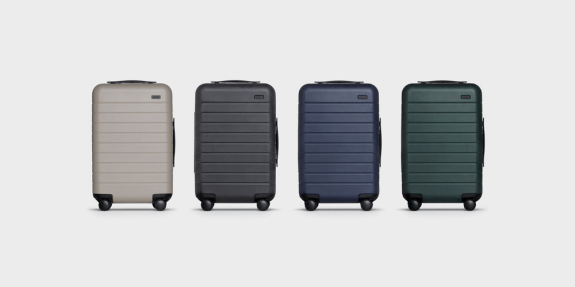 Set of four hard shell suitcases in beige, black, blue, and green on gray background.