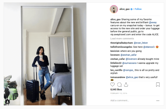 Woman taking a mirror selfie with a suitcase in a bedroom.