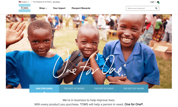 Smiling children in blue shirts, part of TOMS charity program, waving at the camera.