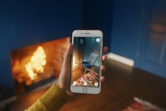 Hand holding smartphone using augmented reality app to view home decor in living room with fireplace.
