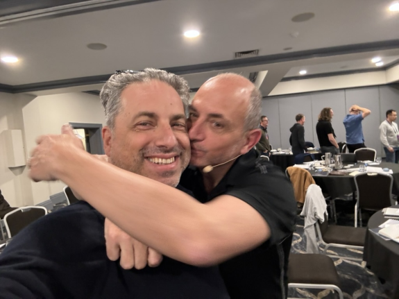 Two men hugging and smiling at a conference room event.