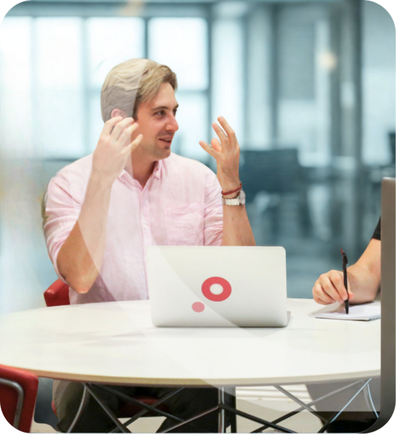 Two people discussing at a round table with a laptop in an office setting.