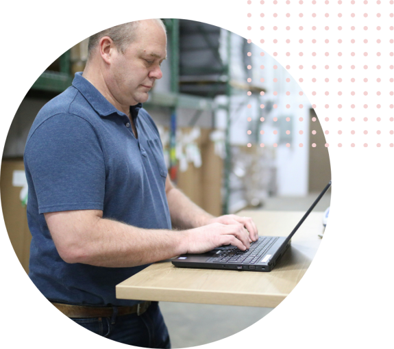 Man in blue shirt working on a laptop at a warehouse desk