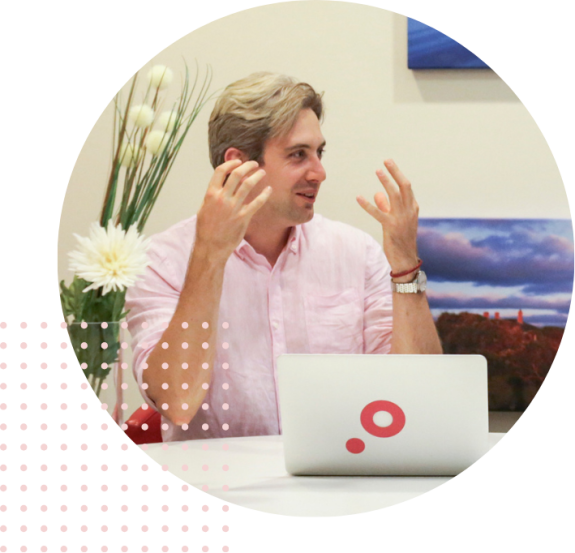 Person in pink shirt talking animatedly at a desk with a laptop