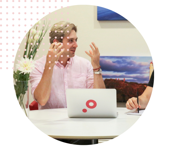 Man in pink shirt discussing work with a laptop during a meeting.