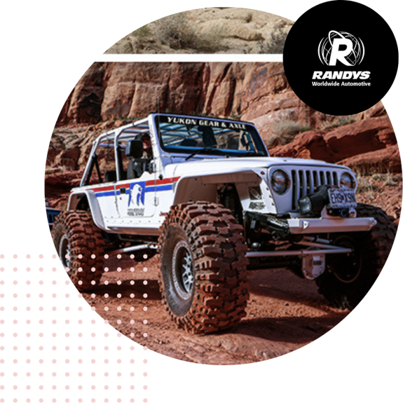 White jeep with large tires off-roading on rocky terrain with Randys logo.