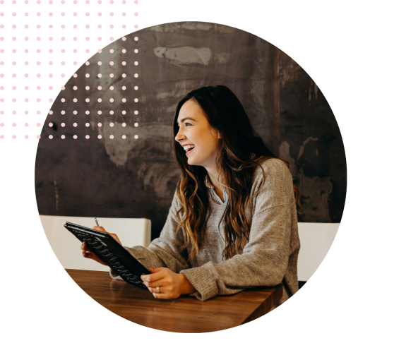 Woman smiling while holding a tablet in a cafe setting.