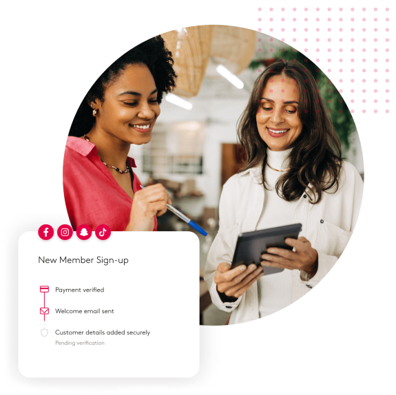 Two women discussing new member sign-up using a tablet in an office setting.